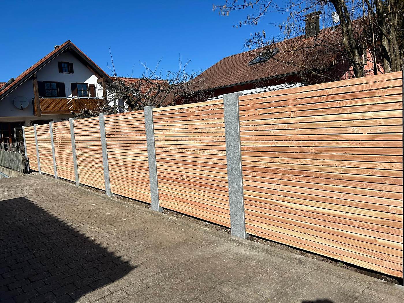 Sichtschutz aus Lärchenholz mit Granitpfosten an einer Einfahrt